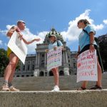 Three people with signs about Roe stand in front of the Pennsylvania capitol building