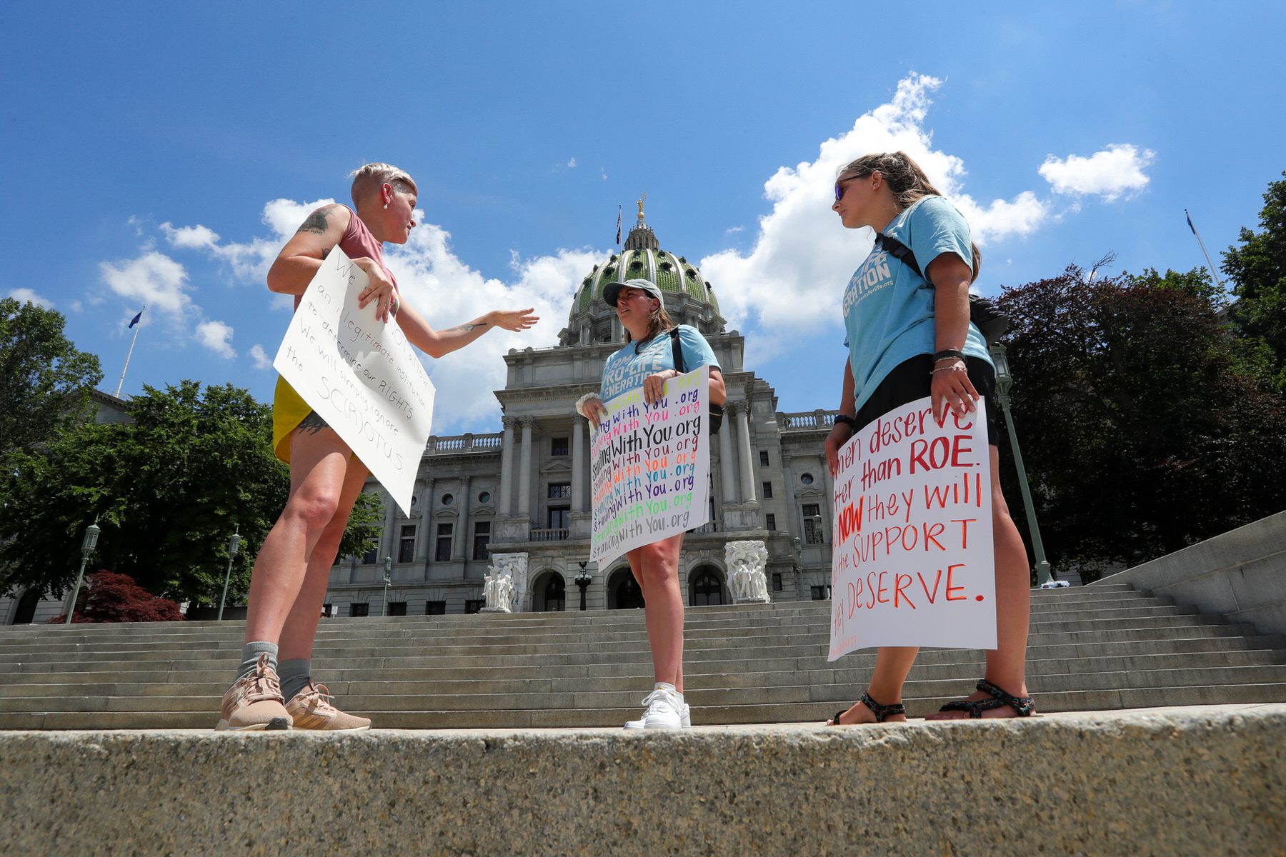 Three people with signs about Roe stand in front of the Pennsylvania capitol building