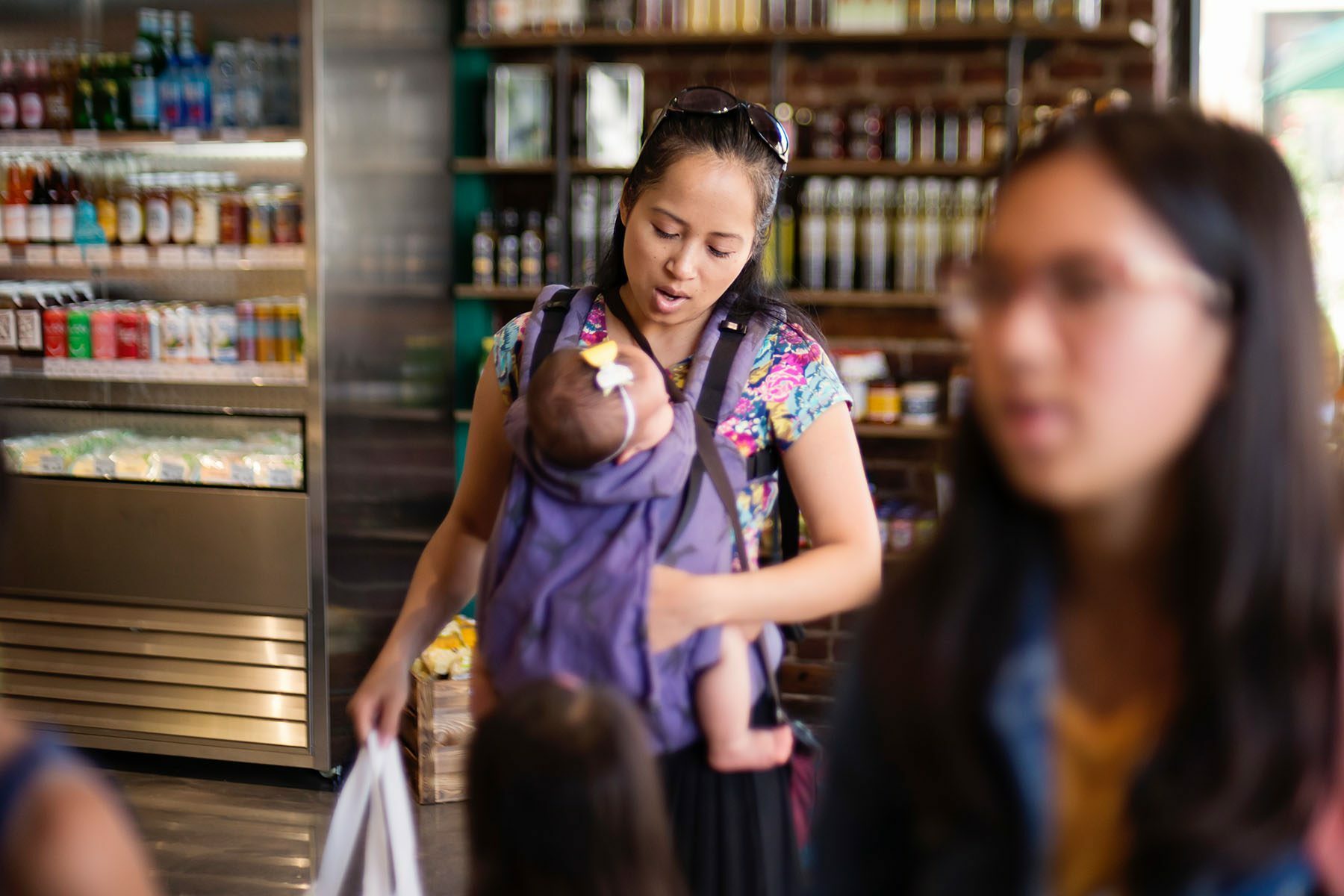 A mother with a baby in a carrier on her chest shops for groceries.