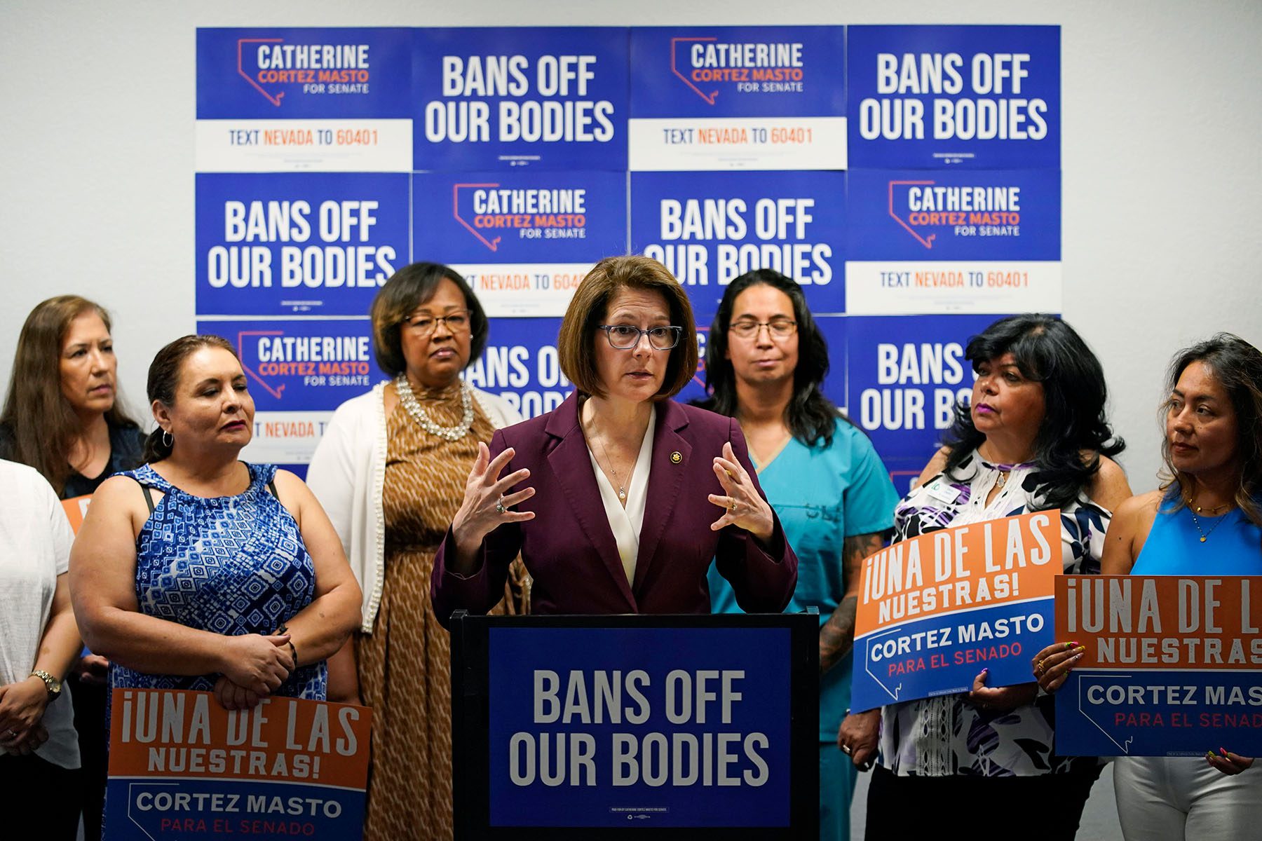 Sen. Catherine Cortez Masto stands behind a podium surrounded by women holding "Bans Off Our Bodies" signs.