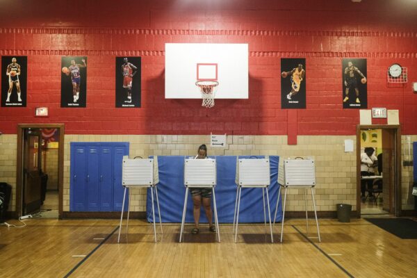 A person votes in a gym with a basketball hoop behind them