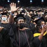 A graduate, surrounded by other graduates in caps and gowns, waives during a commencement ceremony.