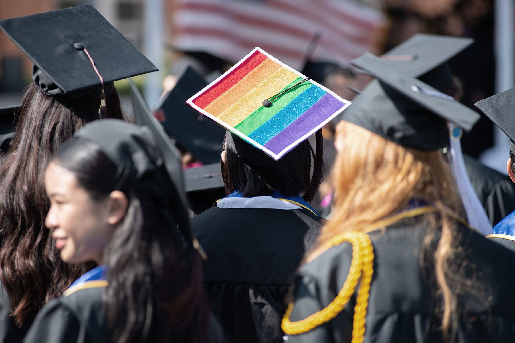 A student sports pride colors on their cap at a college graduation.