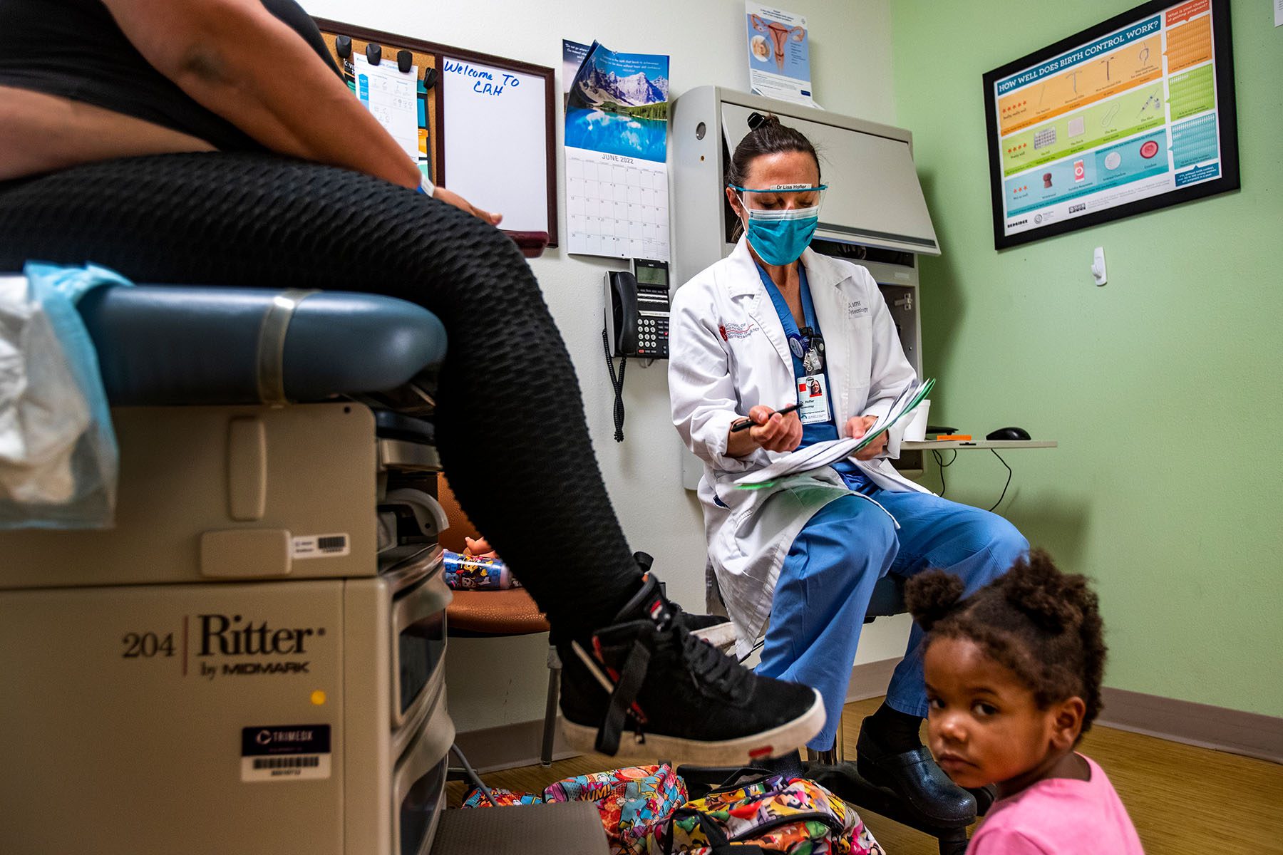 Dr. Lisa Hofler discusses the procedure for getting a medication abortion with a patient as the patient's young daughter sits on the floor.