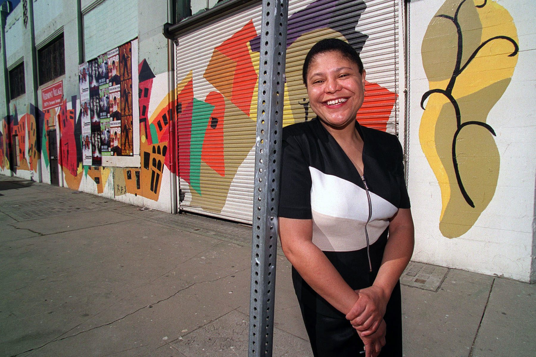 An image of Bass smiling on a Los Angeles street in front of a colorful mural, taken in the early 2000s.