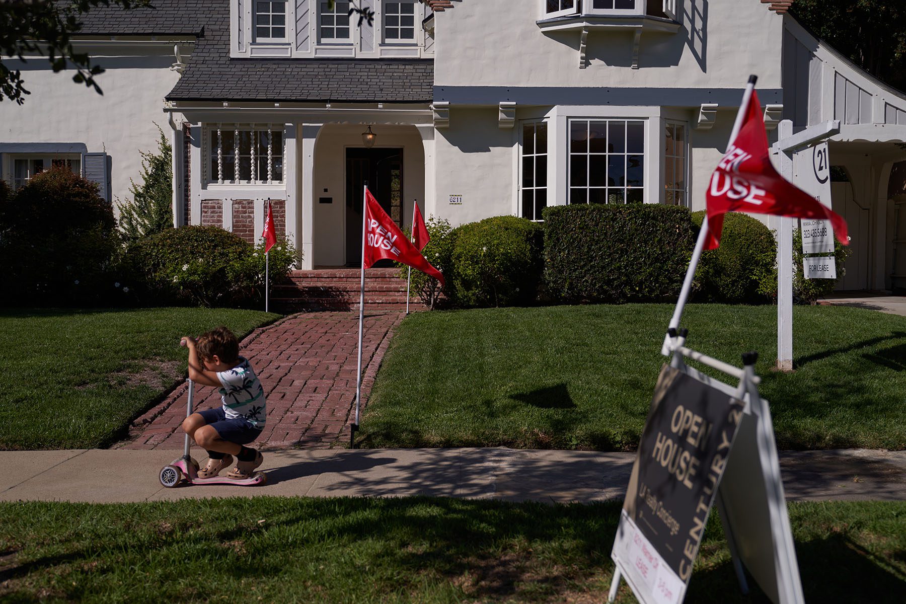 A child rides a scooter past "open house" flags displayed outside a single family home.