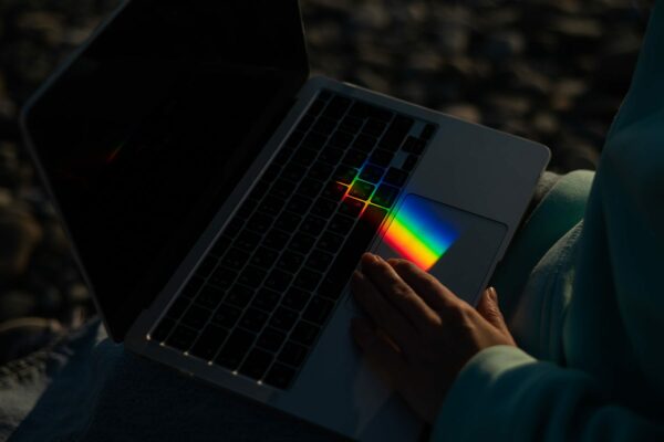 A person uses a laptop on which light is refracted, making a small rainbow appear on the touchpad.