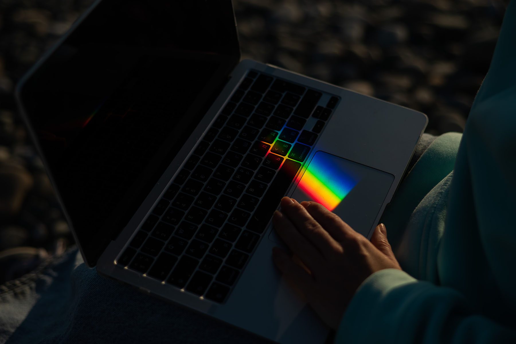 A person uses a laptop on which light is refracted, making a small rainbow appear on the touchpad.