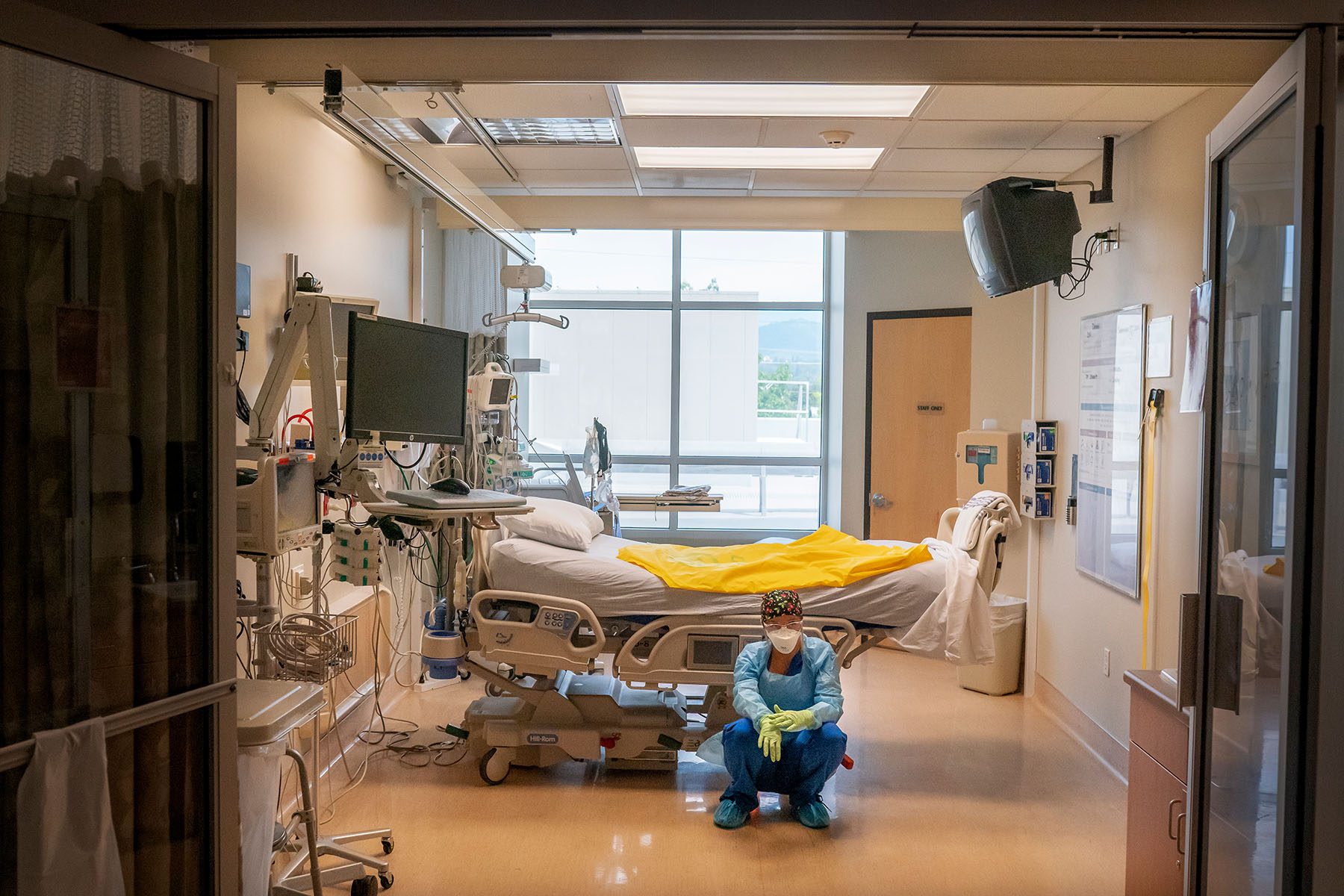 A nurse crouches on the floor near an empty bed as she waits for her next COVID-19 case to be brought in from the emergency room.