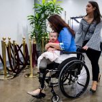 Sen. Tammy Duckworth holds her daughter Maile as they both smile. A woman pushes Sen. Duckworth's wheelchair.