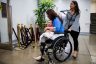 Sen. Tammy Duckworth holds her daughter Maile as they both smile. A woman pushes Sen. Duckworth's wheelchair.