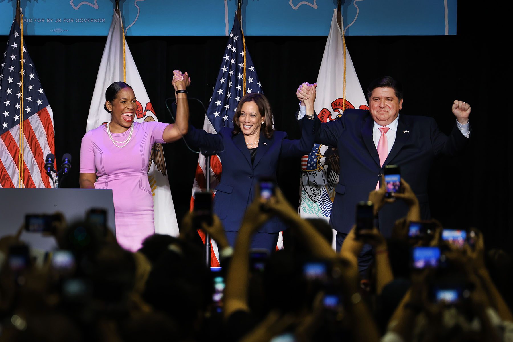 Kamala Harris, Lt. Governor Juliana Stratton and Governor J.B. Pritzker hold hands and salute the crowd from a stage.