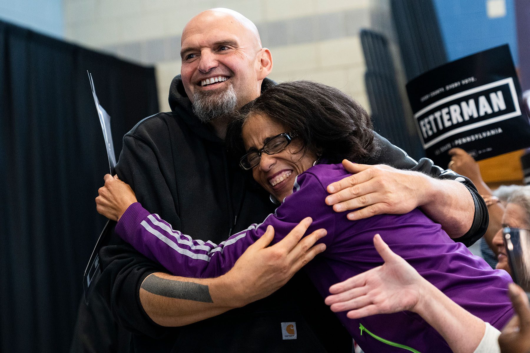 John Fetterman hugs a smiling supporter during a rally.