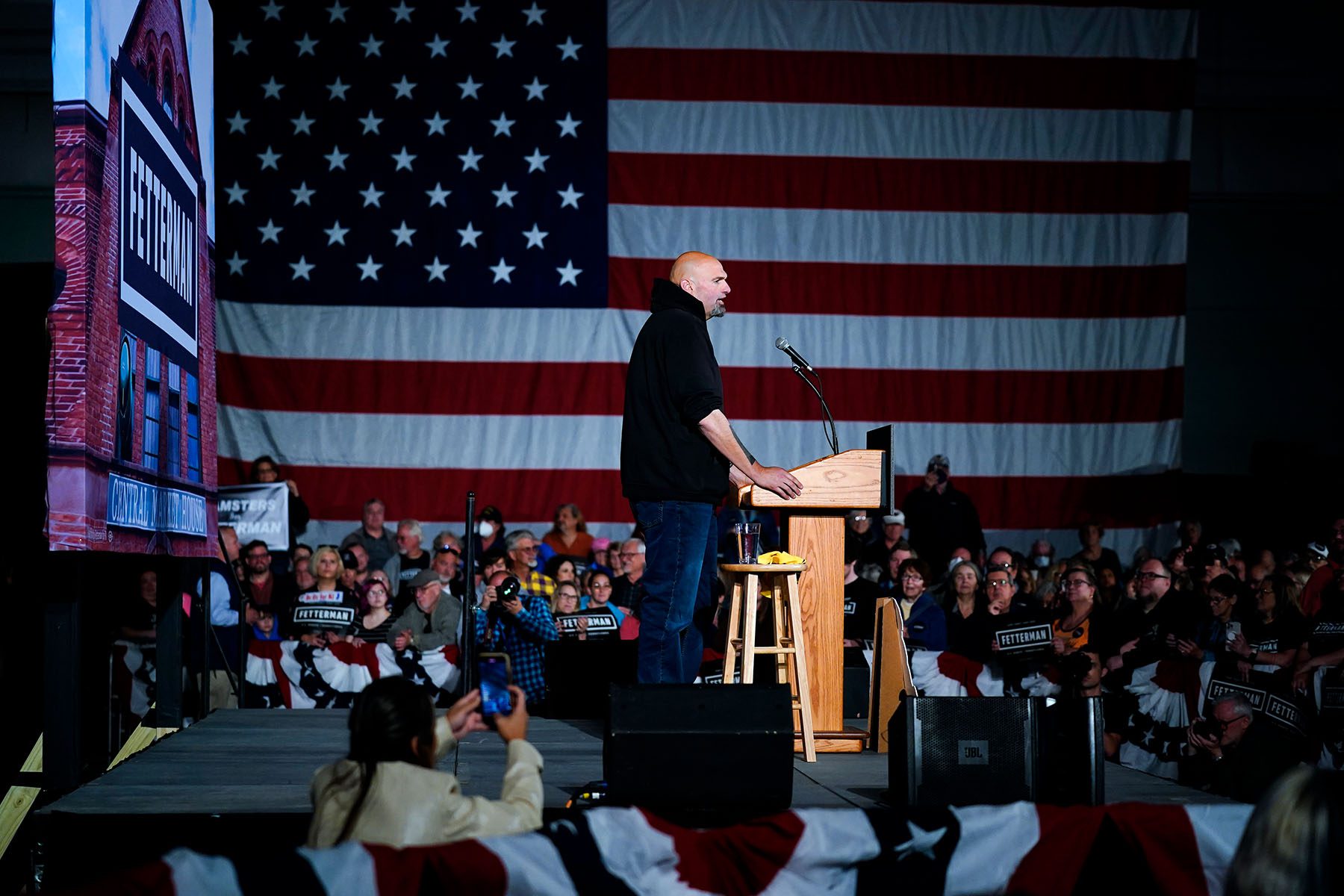 John Fetterman stands at a podium surrounded by supporters during a campaign event.