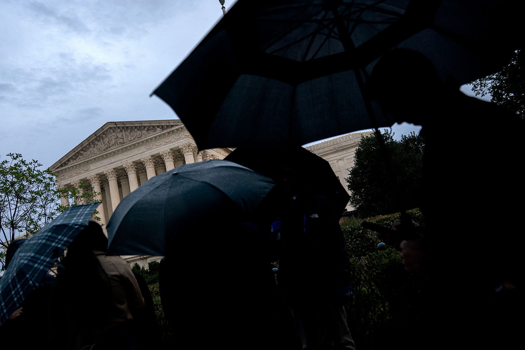 People holding black umbrellas wait in line outside the Supreme Court building on a rainy day.