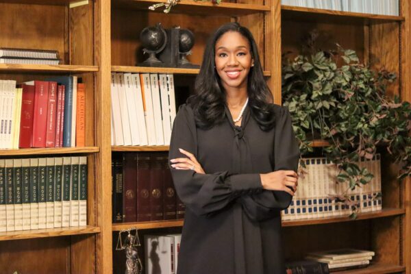 Kyra Harris Bolden stands in front of a bookcase wearing black with arms folded