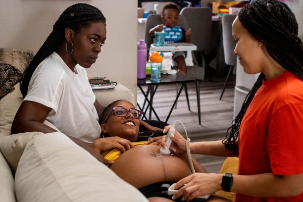 Midwife Angie Miller listens to a baby's heartbeat while speaking to her client and her partner.