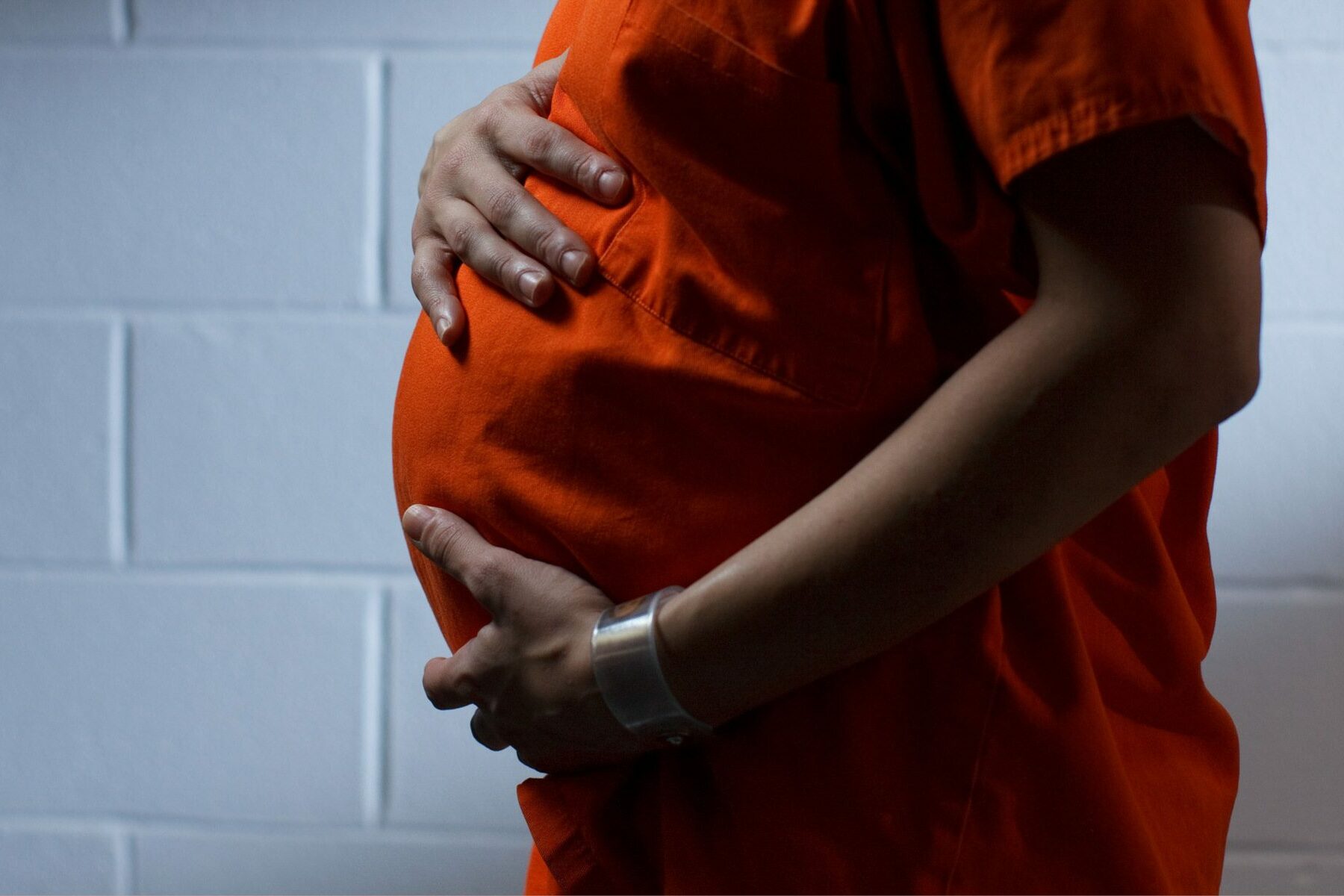 person in orange jumpsuit holds pregnant belly