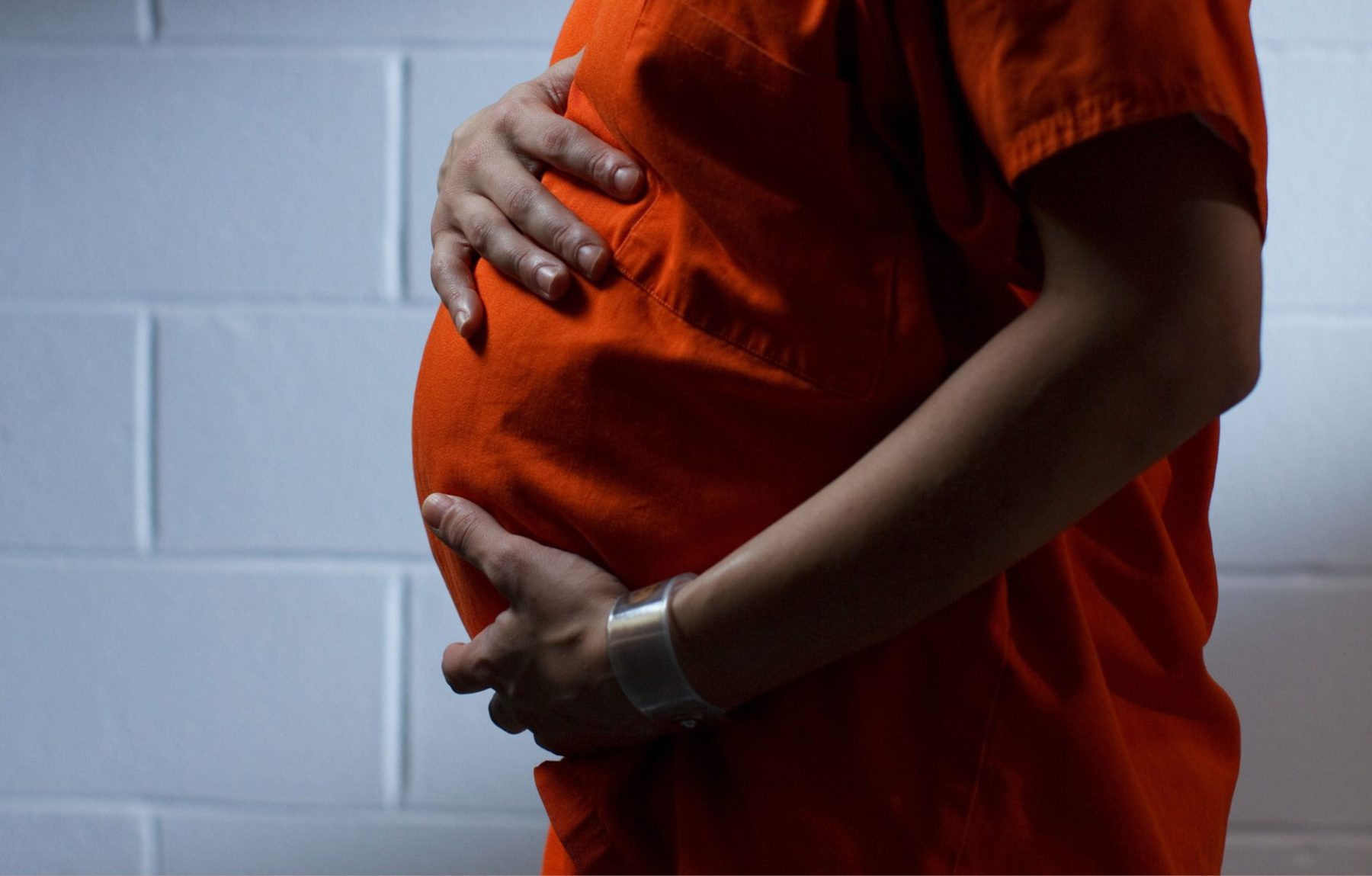 person in orange jumpsuit holds pregnant belly