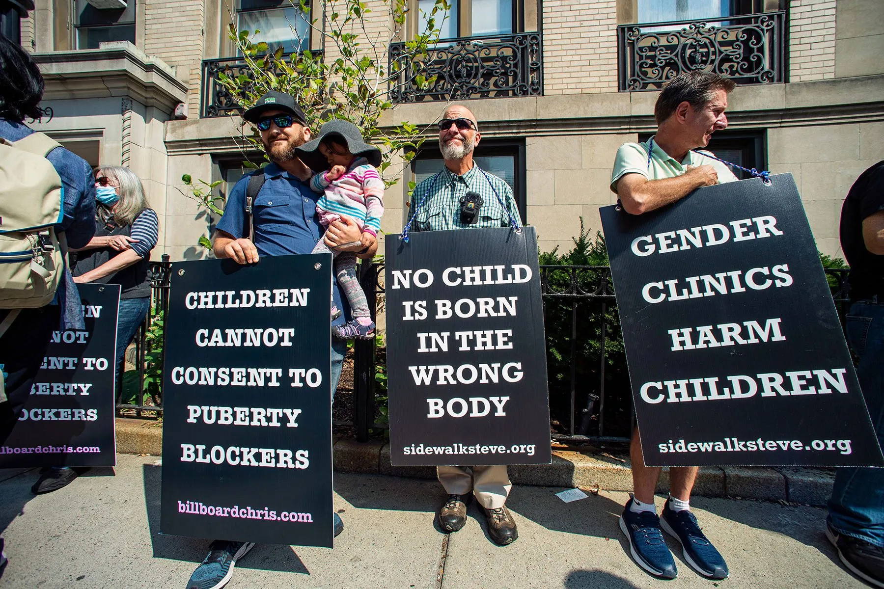 Anti-trans activists wear signs that read "children cannot consent to puberty blockers," "no child is born in the wrong body," and "gender clinics harm children" outside Boston Children's Hospital.