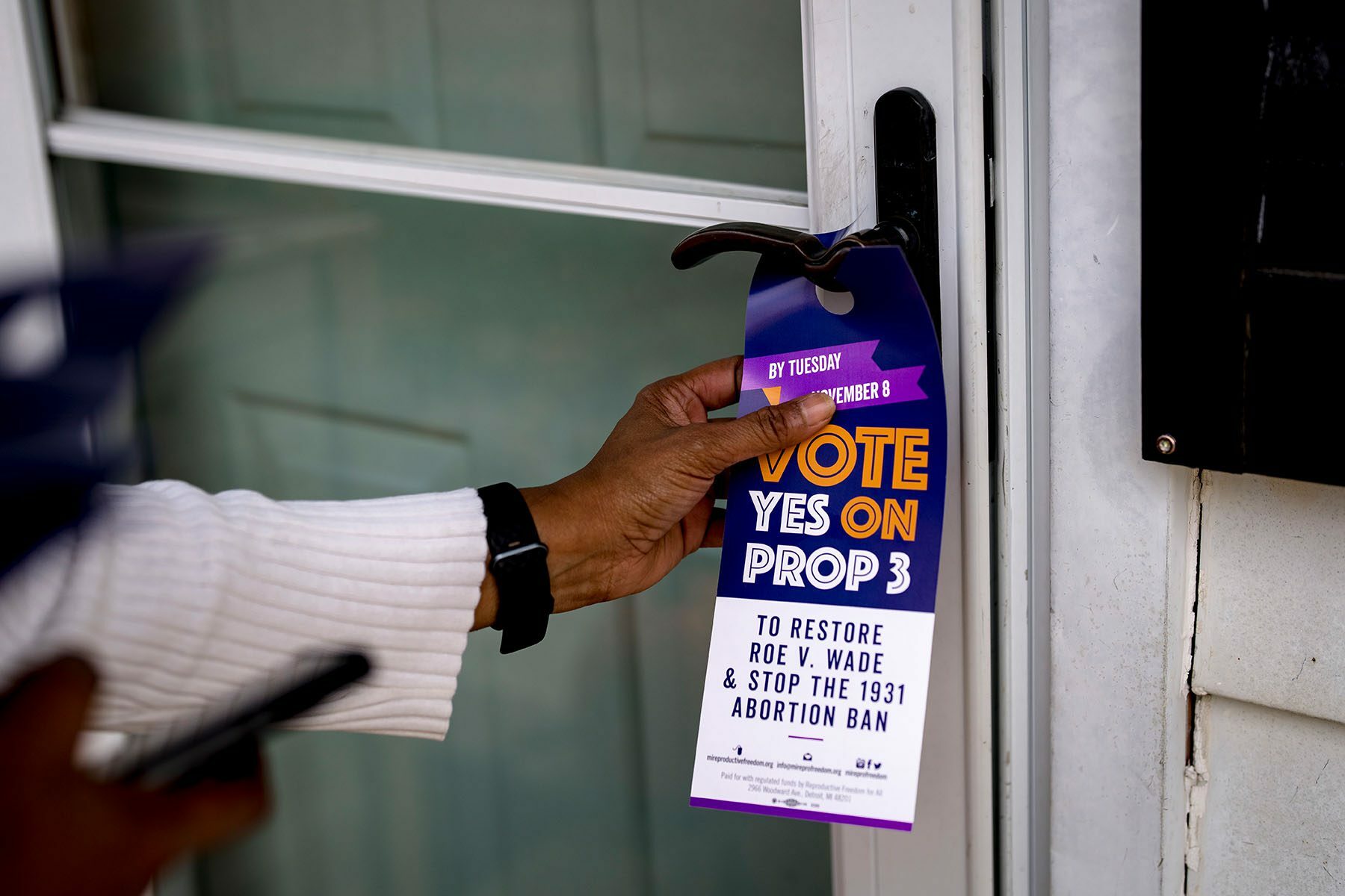 A volunteer places a door tag in support of Proposal 3 on a door. The tag read 