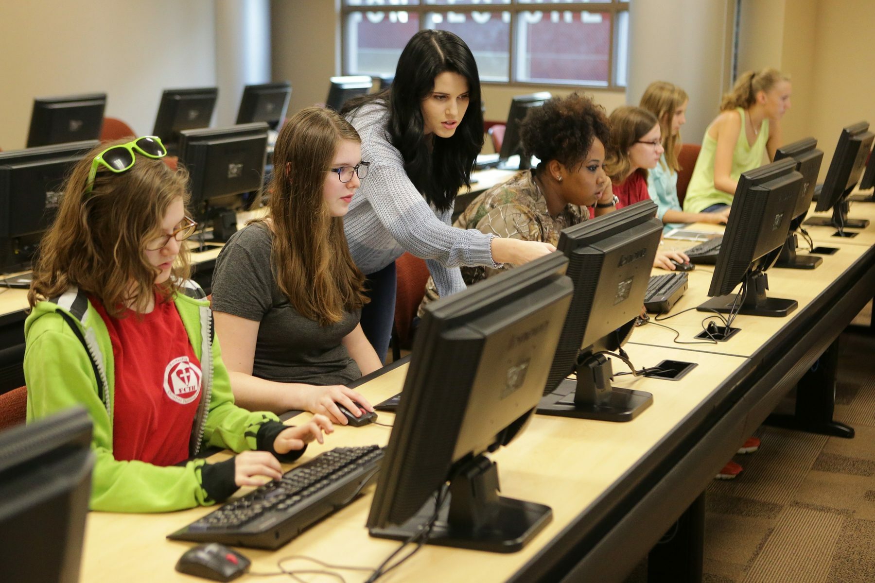 A woman stands and teaches students in a room full of computers.