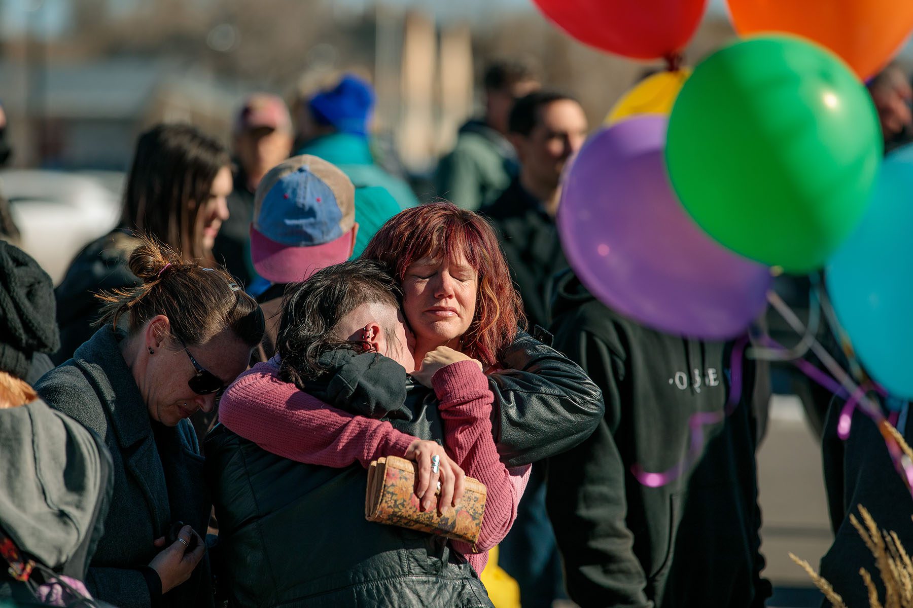 Tearful people embrace outside a vigil at All Souls Unitarian Church. Rainbow colored balloons can be seen in the foreground.