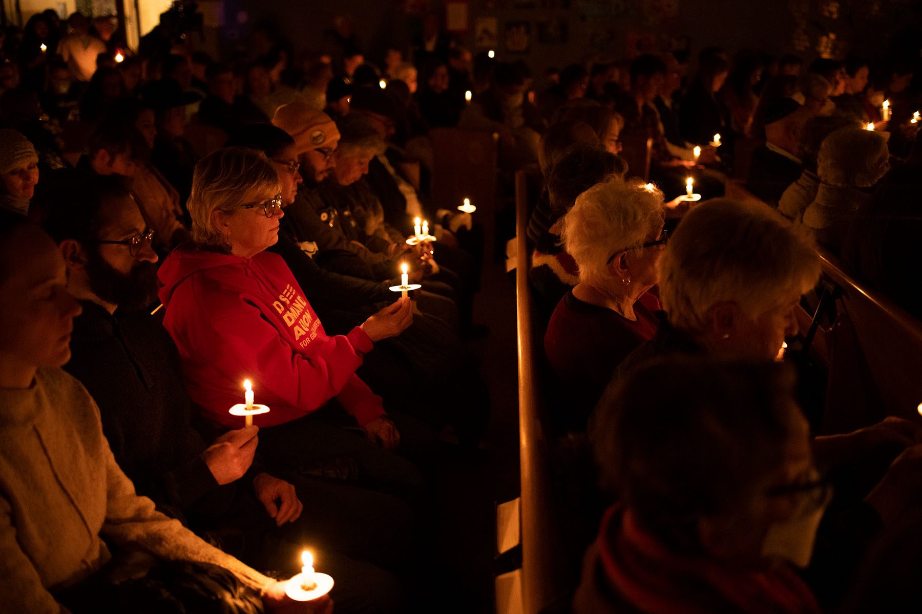 People sit in pews and hold candles during a vigil at Temple Beit Torah.