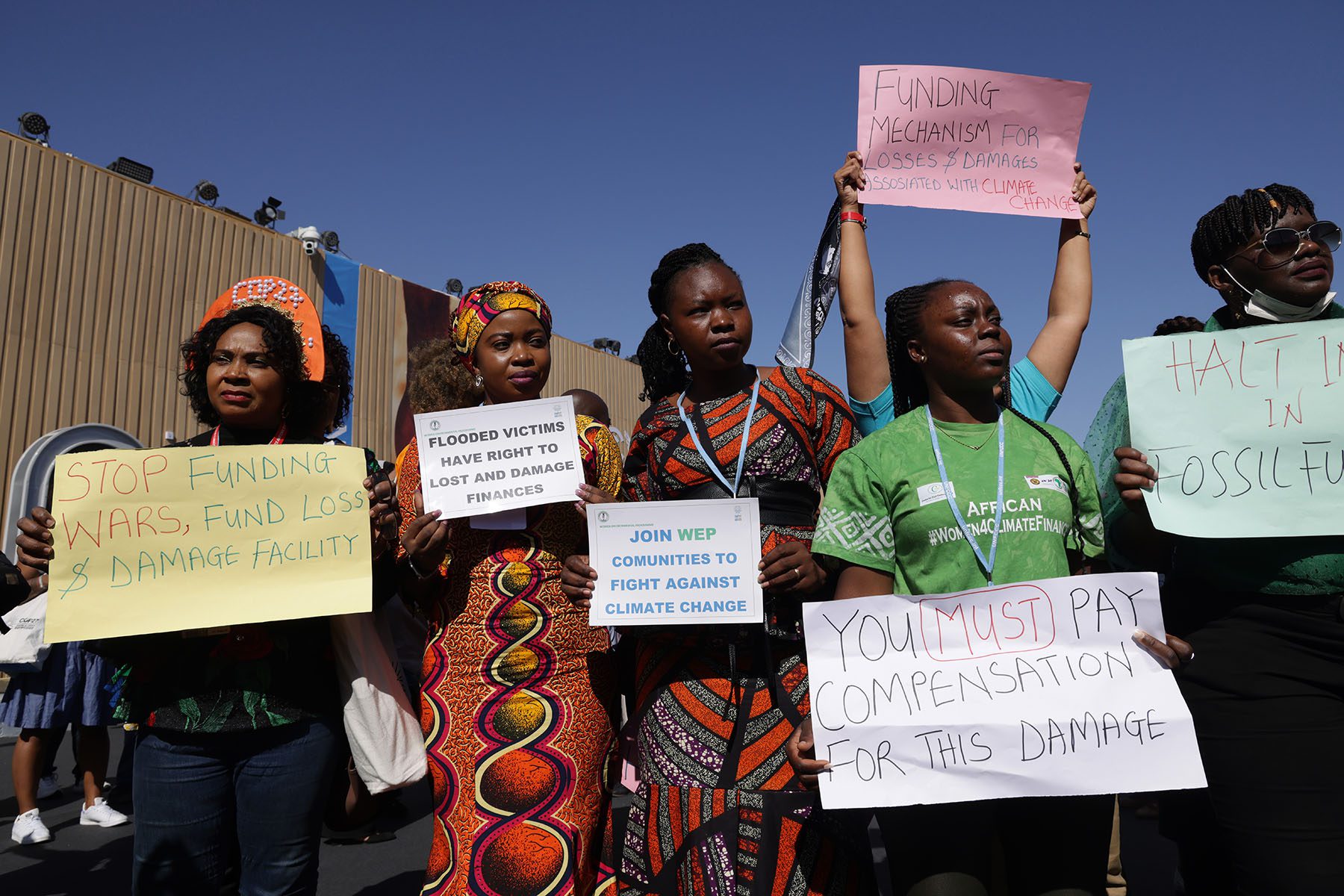 African activists hold signs that read "you must pay compensation for this damage" and "funding mechanism for losses & damages accocoated with climate change"