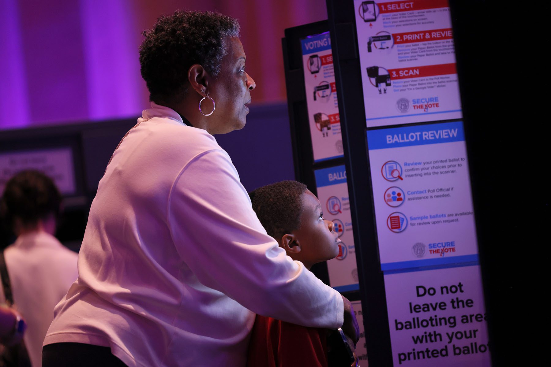 A woman casts her vote while holding a child at Fox Theatre in Atlanta. The child's face is illuminated by the electronic voting screen.