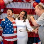 Monica De La Cruz and a supporter wearing an American flag shirt pose in front of red, white and blue balloons at her election night party.