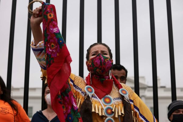 A demonstrator in indigenous garb holds up her fist in front of the White House.