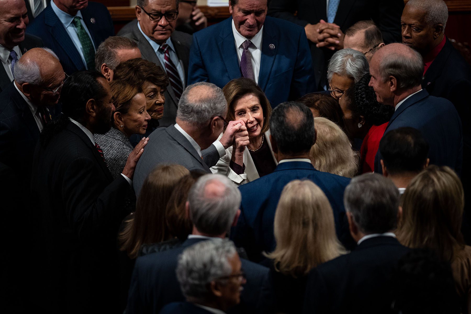 Nancy Pelosi holds Chuck Schumer's hand against her cheek as lawmakers surround her to greet her after she announced she is stepping down from her leadership position.
