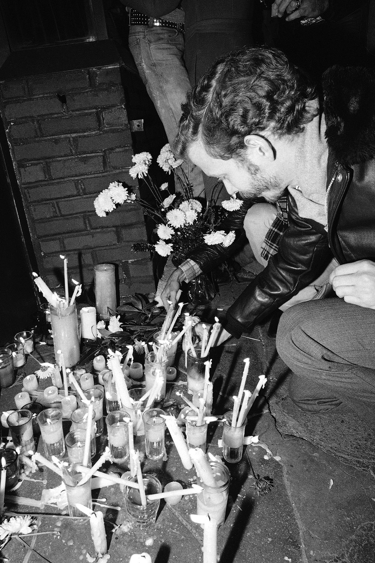 A man places a memorial candle in front of the Ramrod Bar in New York City. Dozen of candles and flowers are on the ground.