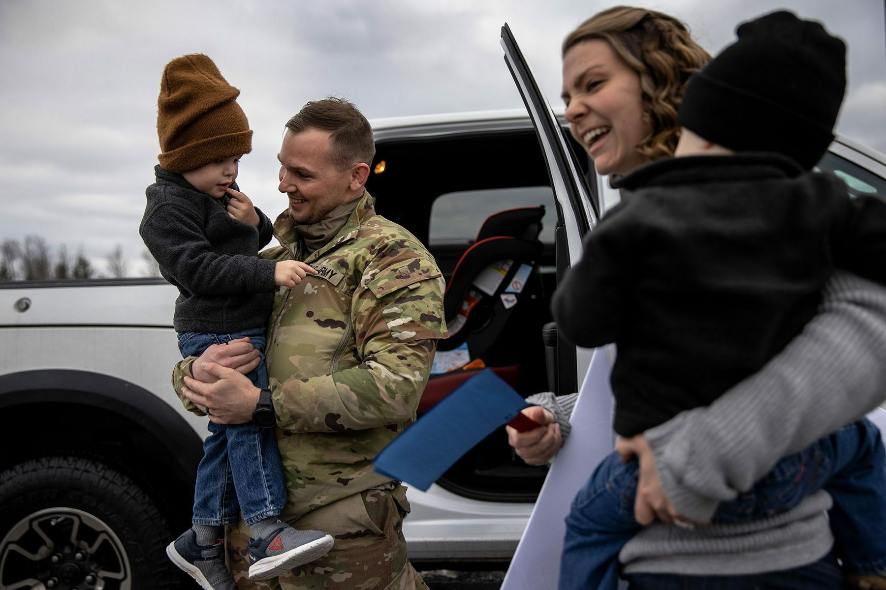 A U.S. Army Staff Sargent holds his son in his arms and smiles as his spouse holds their other child.