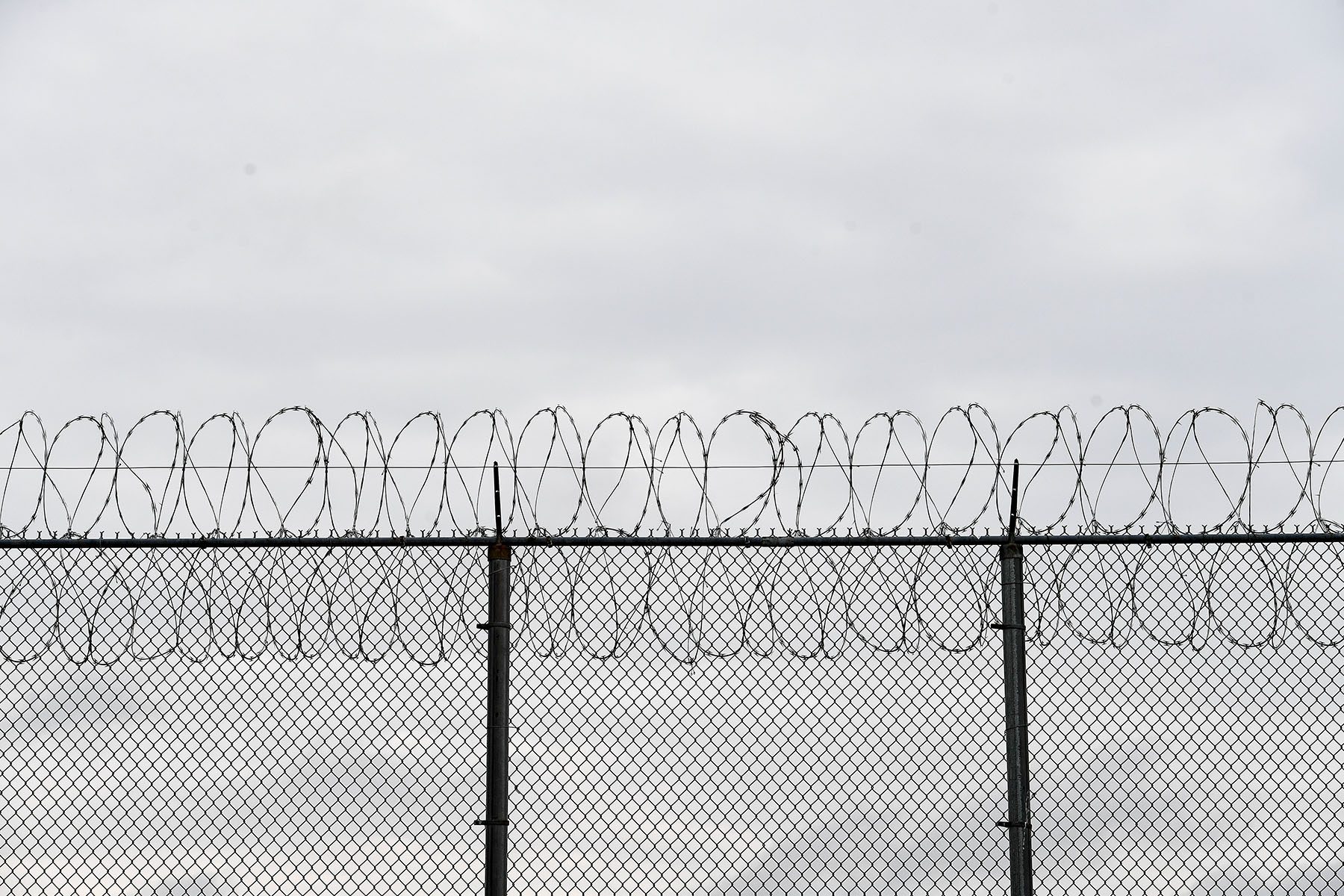 A prison fence with barbed wire photographed on a cloudy day.