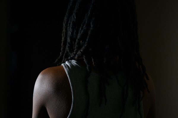 A black woman photographed in a dark room with her back to the camera.