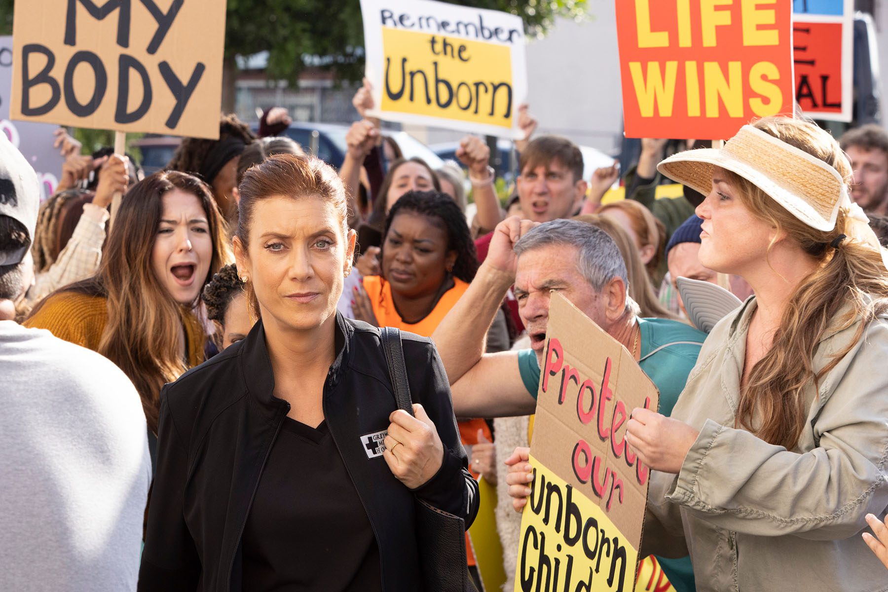 Still from an episode of TV show Grey's Anatomy in which a character is seen walking through a crowd of anti-abortion protesters.