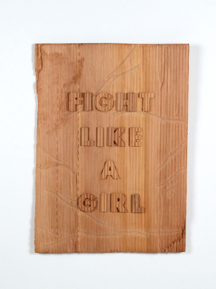 A carved, wooden protest sign that reads "fight like a girl."