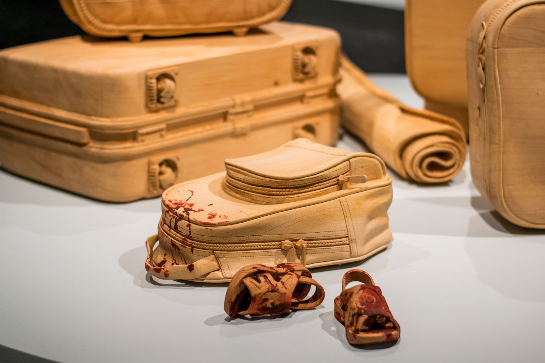 A collection of carved, wooden luggage with a pair of bloody children's shoes.