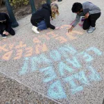 Children write on a sidewalk in blue and orange chalk to promote paid leave.