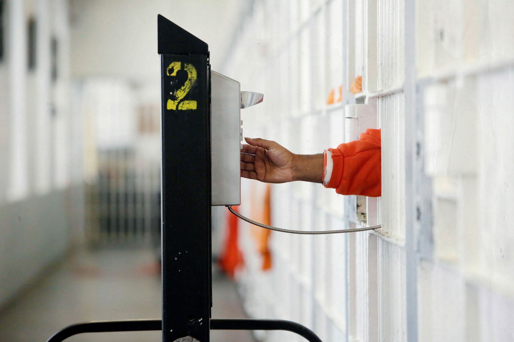 An inmate's hand is seen peeking out their cell as they dial a rollaway phone at a San Francisco jail.
