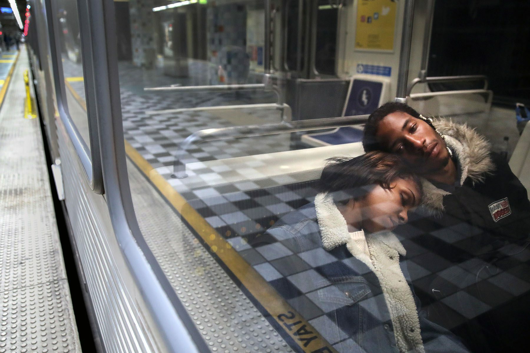 A woman rests on a man's shoulder as they ride a Los Angeles Metro Rail train.