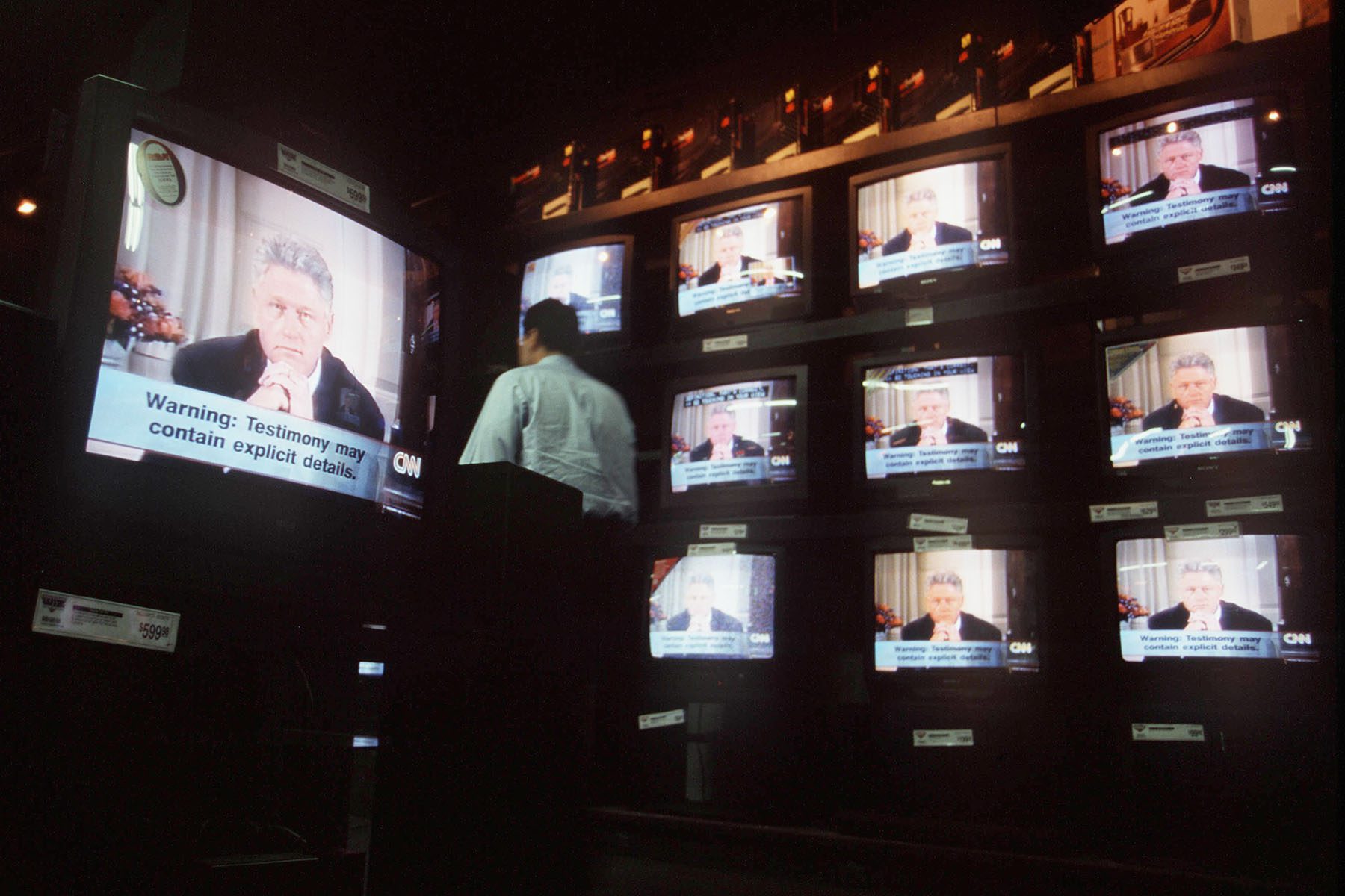 A person stands in front of multiple television monitors broadcasting President Bill Clinton's Grand Jury testimony on the Monica Lewinsky affair in an electronics store.