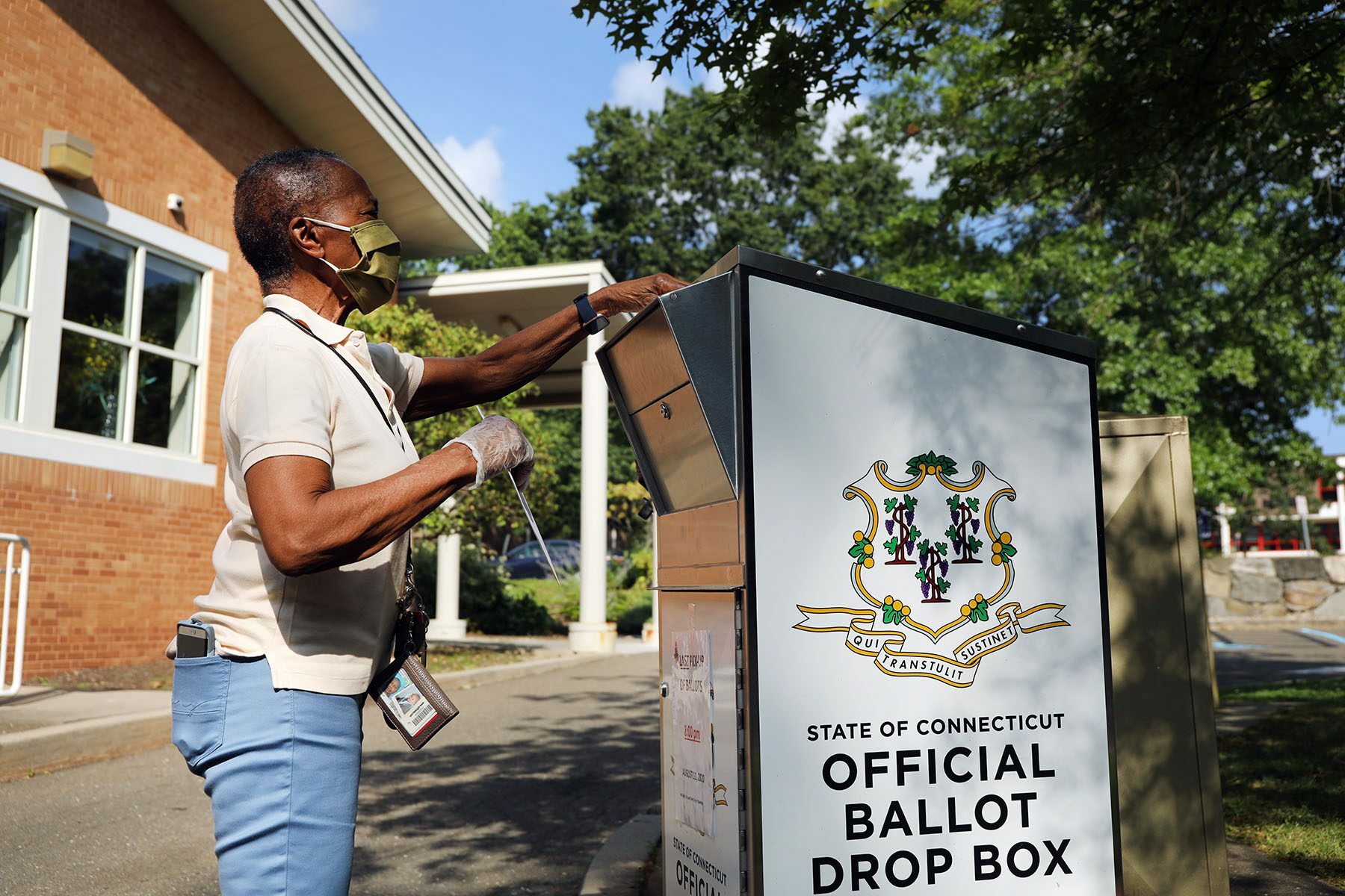 A voter drops her primary ballot at a secure ballot drop box outside a library.