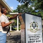 A voter drops her primary ballot at a secure ballot drop box outside a library.