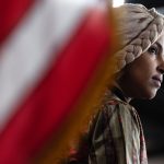 Rep. Ilhan Omar looks on near an American flag during a news conference.