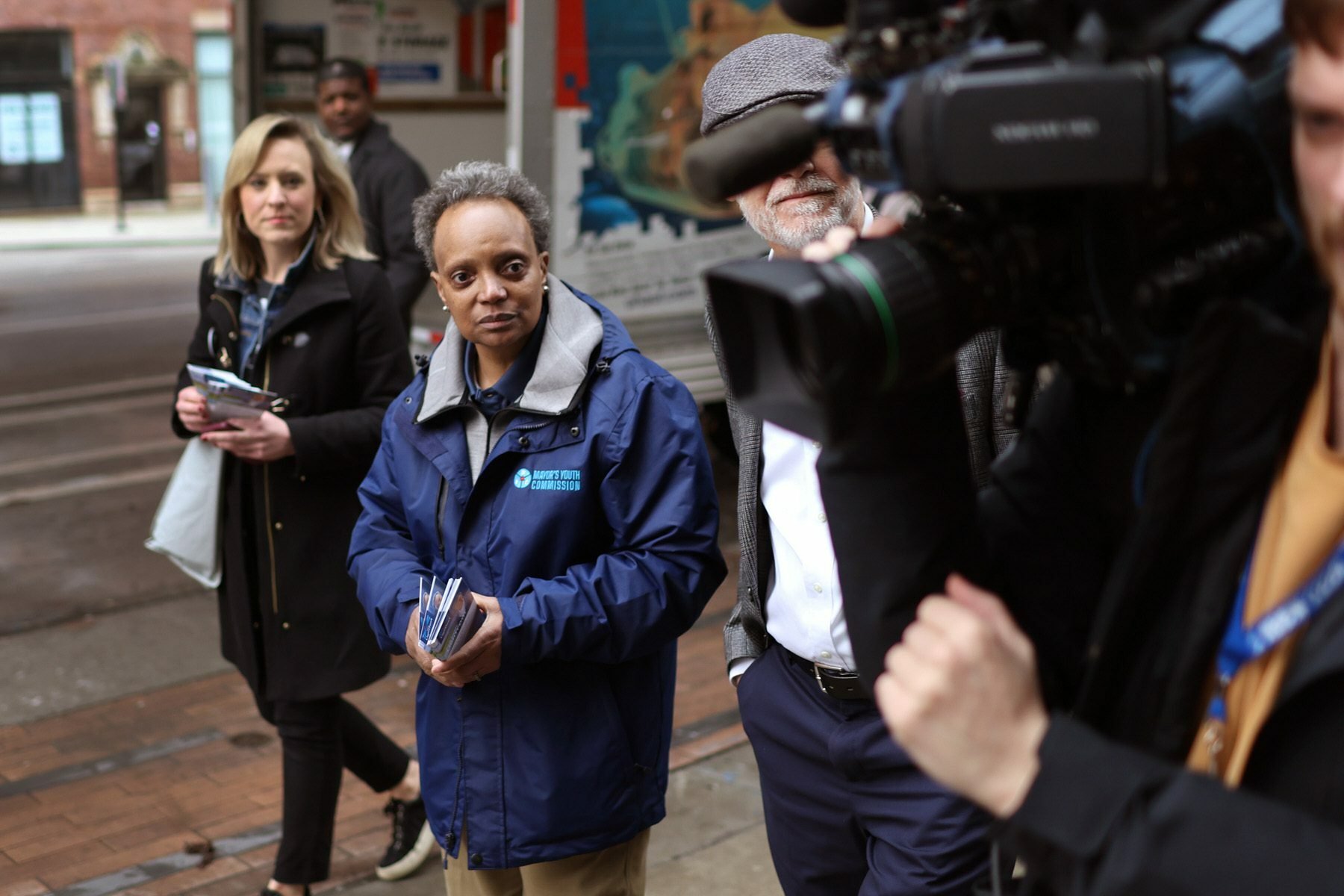 Chicago Mayor Lori Lightfoot walks on a city street with a man holding a camera in the foreground