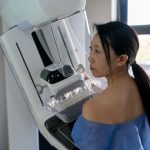 Asian female patient at a hospital getting a mammogram exam wearing a hospital gown and looking serious.