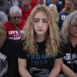 Three women are seen closing their eyes in prayer prior to a rally featuring former President Trump.